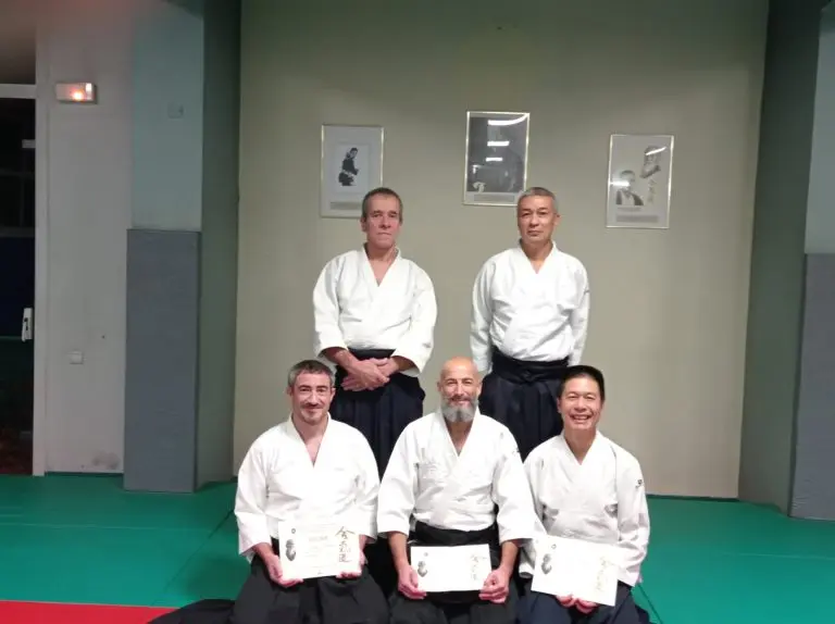 Cinq membres du club en keikogi au dojo, dont trois tiennent leur diplôme